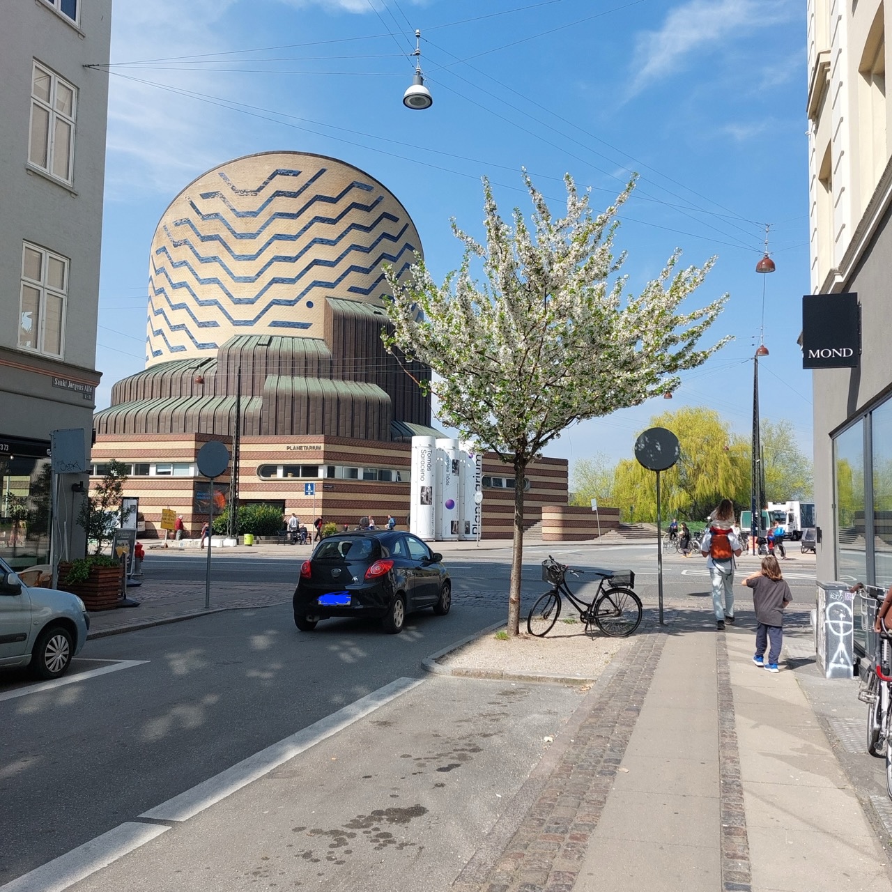 The cylindrical brick façade of the Tycho Brahe Planetarium in Copenhagen, mirrored in the lake beside it under a bright spring sky