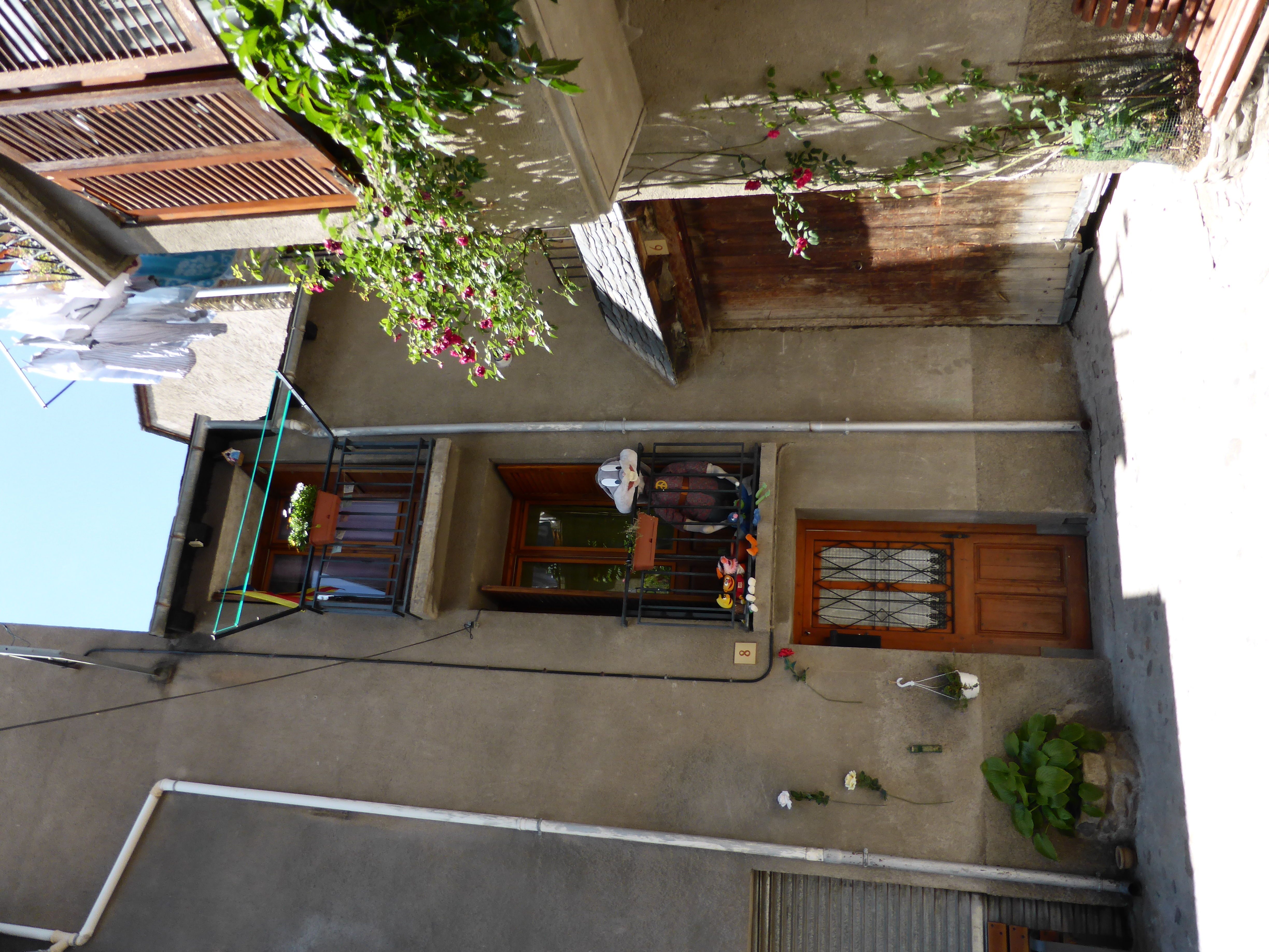 A quiet village street in Salardú with stone houses, wooden shutters, an ornate iron balcony with drying laundry, and a wall of climbing pink roses