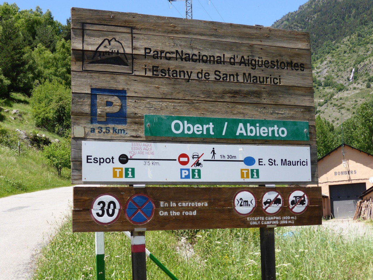 A large wooden park entrance sign for Parc Nacional d'Aigüestortes i Estany de Sant Maurici, showing 'Obert / Abierto' (open), distances from Espot to Sant Maurici, and speed and access restrictions