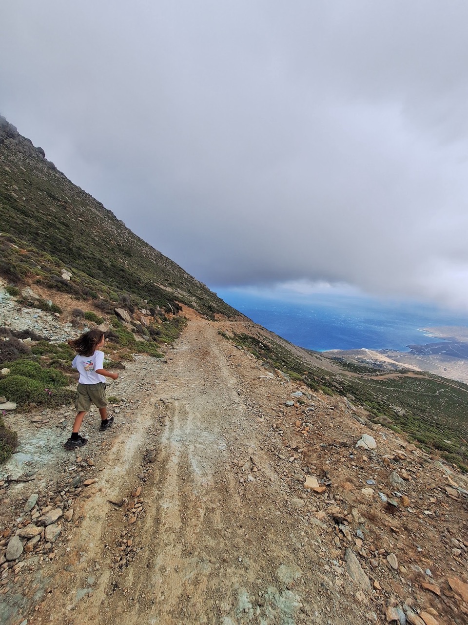 A child climbing the rocky ridge of Mount Tsiknias in Tinos with the sea visible below